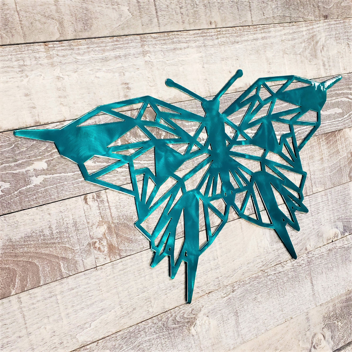 geometric representation of a butterfly with a brushed aqua color finish on a wooden background