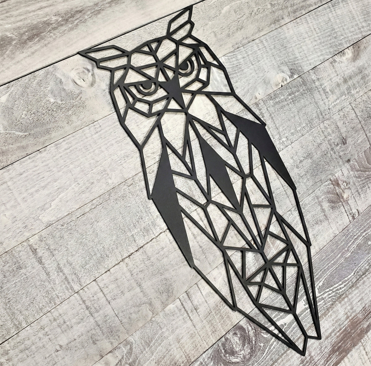 Black geometric owl metal wall art on a wooden background
