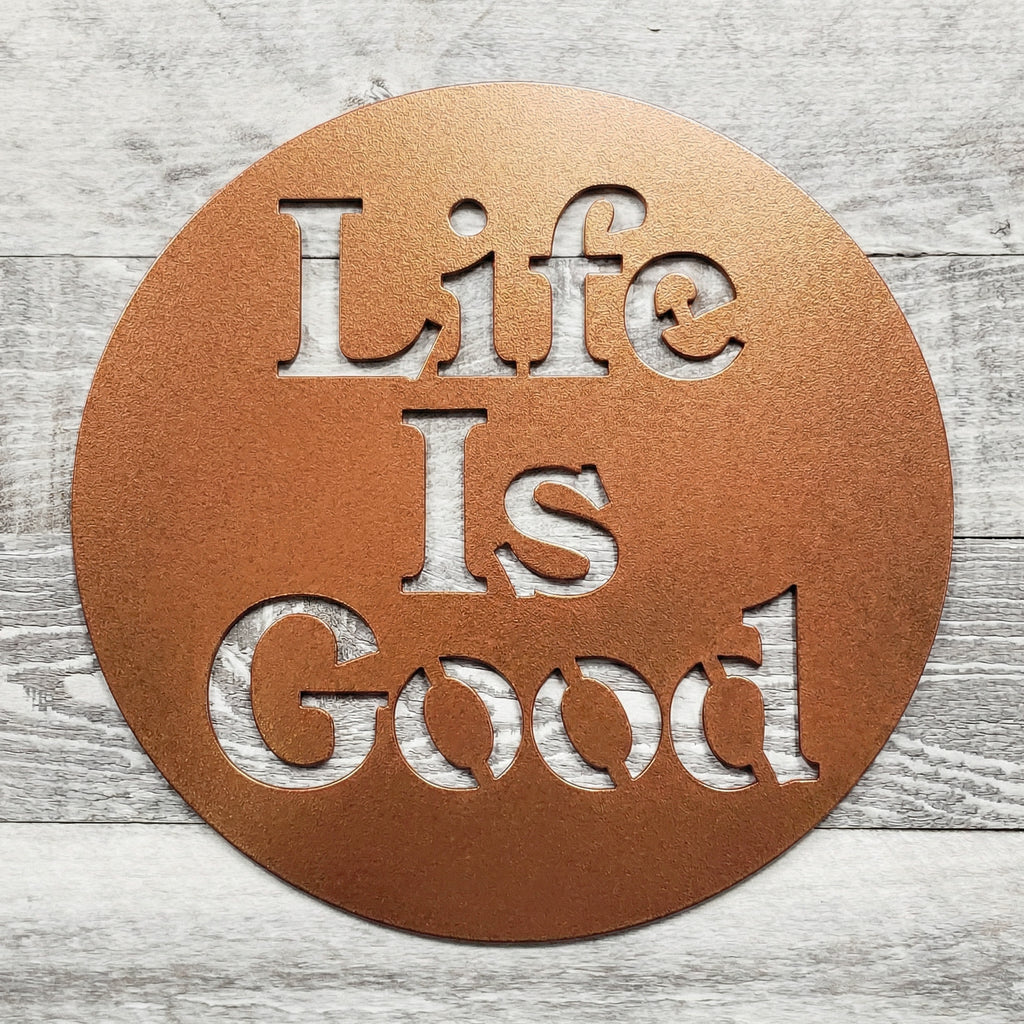 Round metal sign with 'Life Is Good' text on a wooden surface