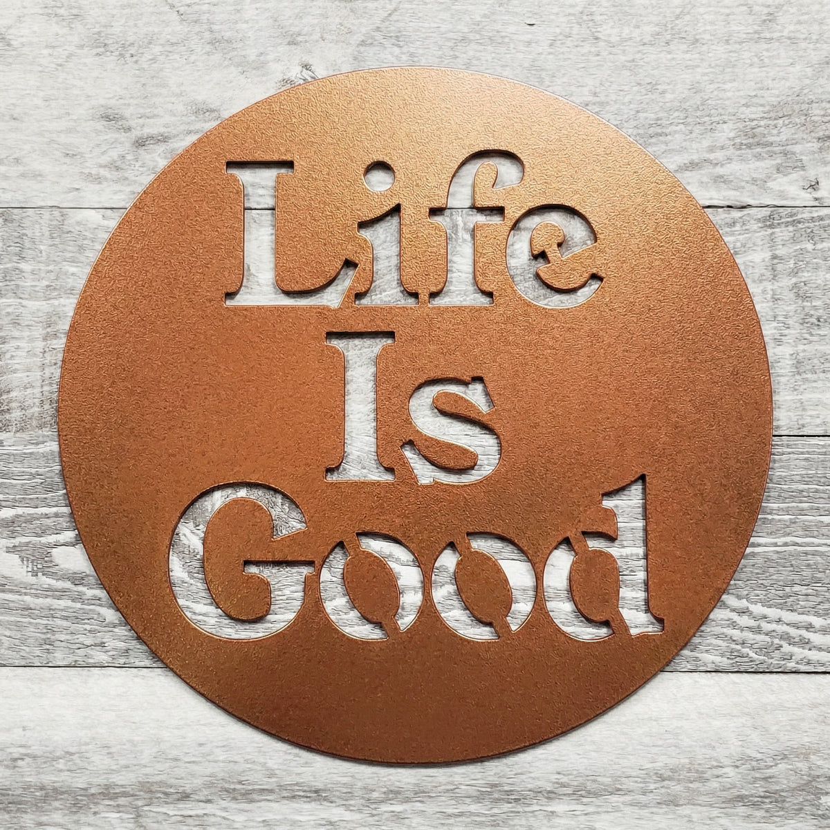 Round metal sign with 'Life Is Good' text on a wooden surface