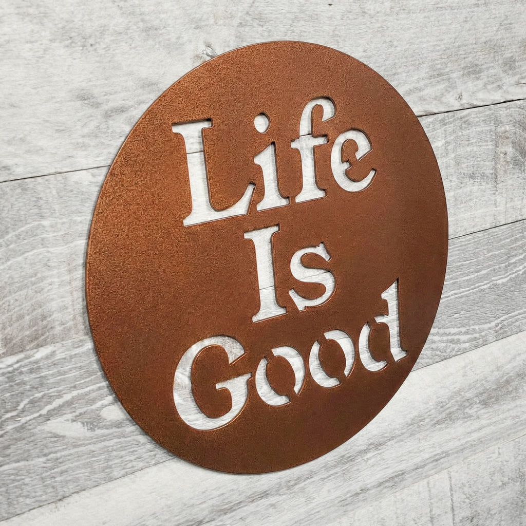 Round metal sign with 'Life Is Good' text on a wooden surface