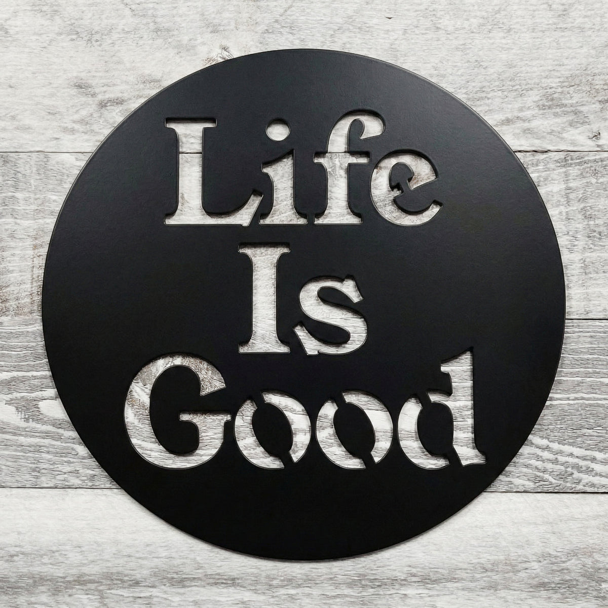 Round black sign with 'Life Is Good' text on a wooden surface