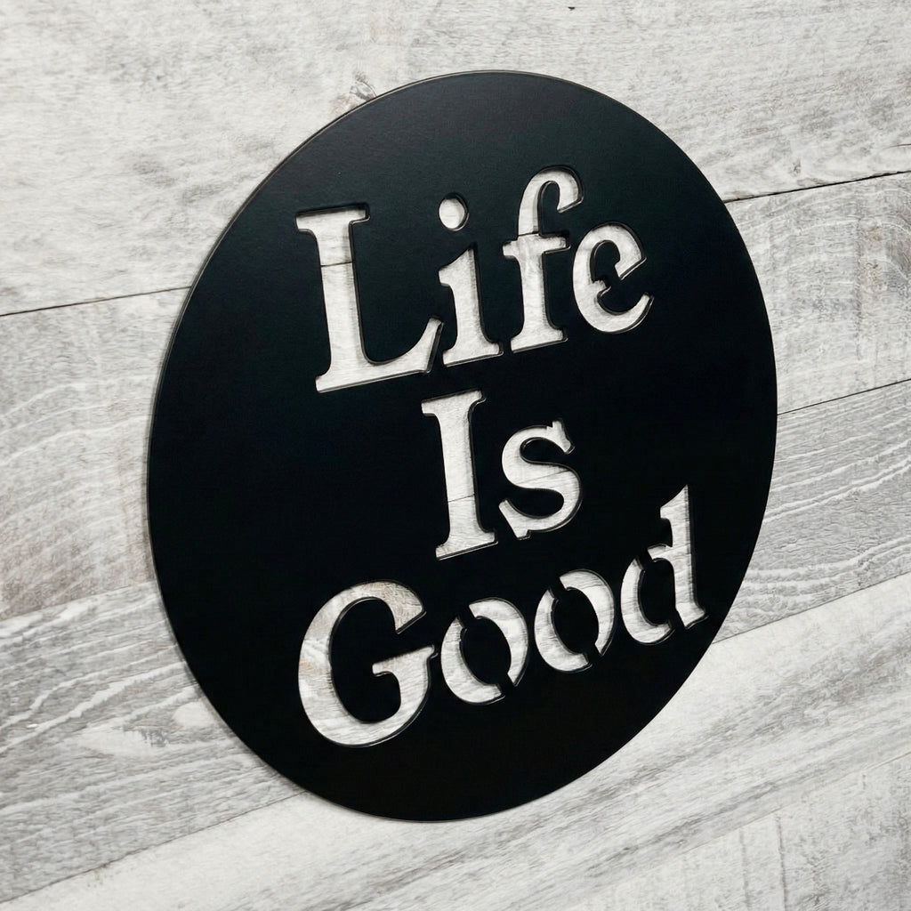 Round black sign with 'Life Is Good' text on a wooden surface