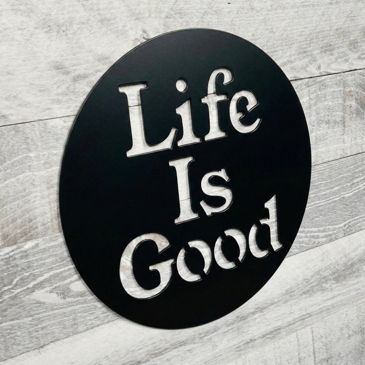 Round black sign with 'Life Is Good' text on a wooden surface