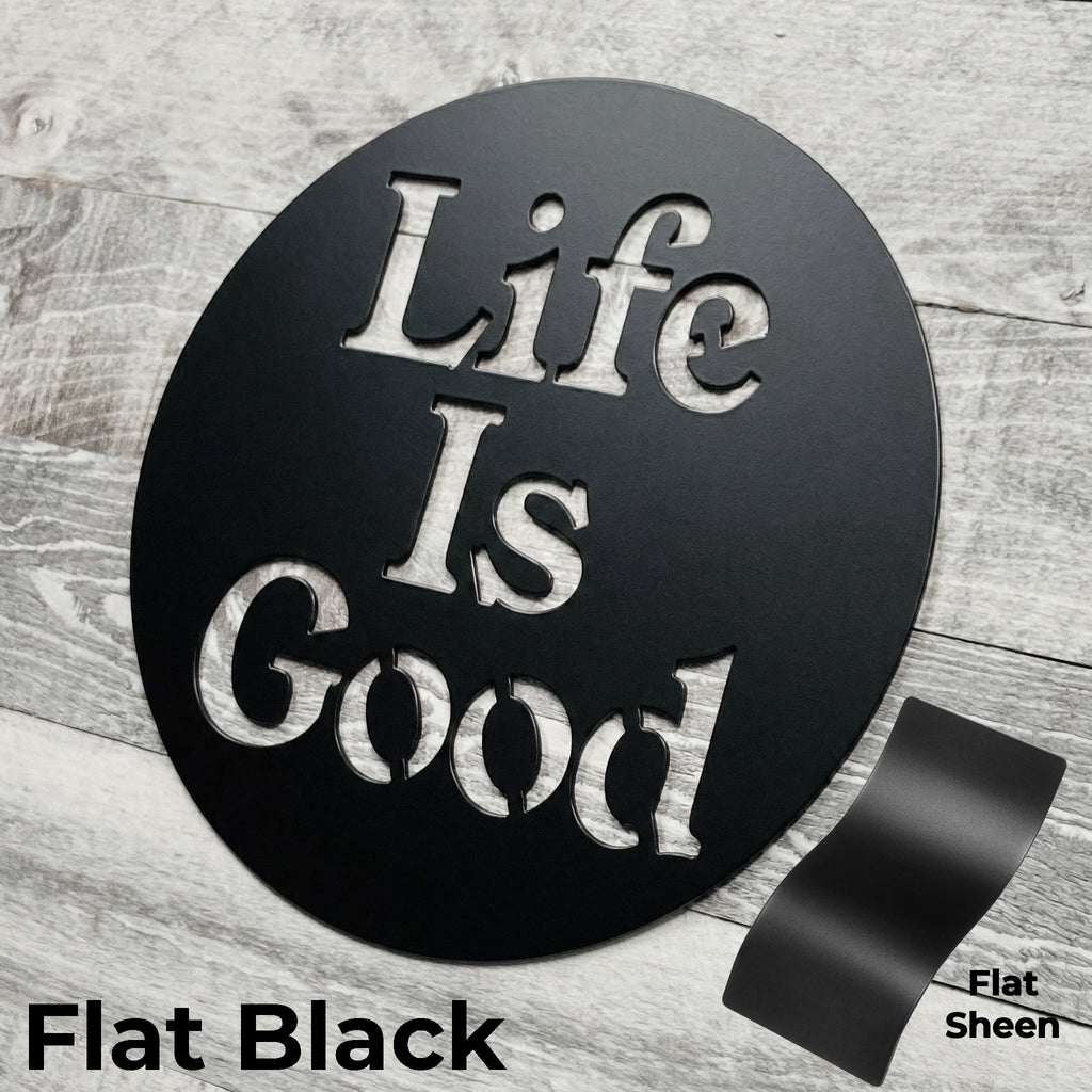 Round black metal sign with 'Life Is Good' text on a wooden surface
