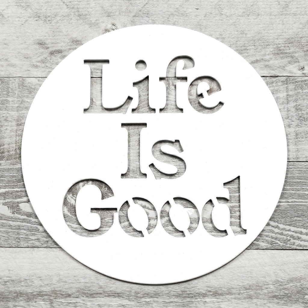 white circular metal sign with 'Life Is Good' text on a wooden background