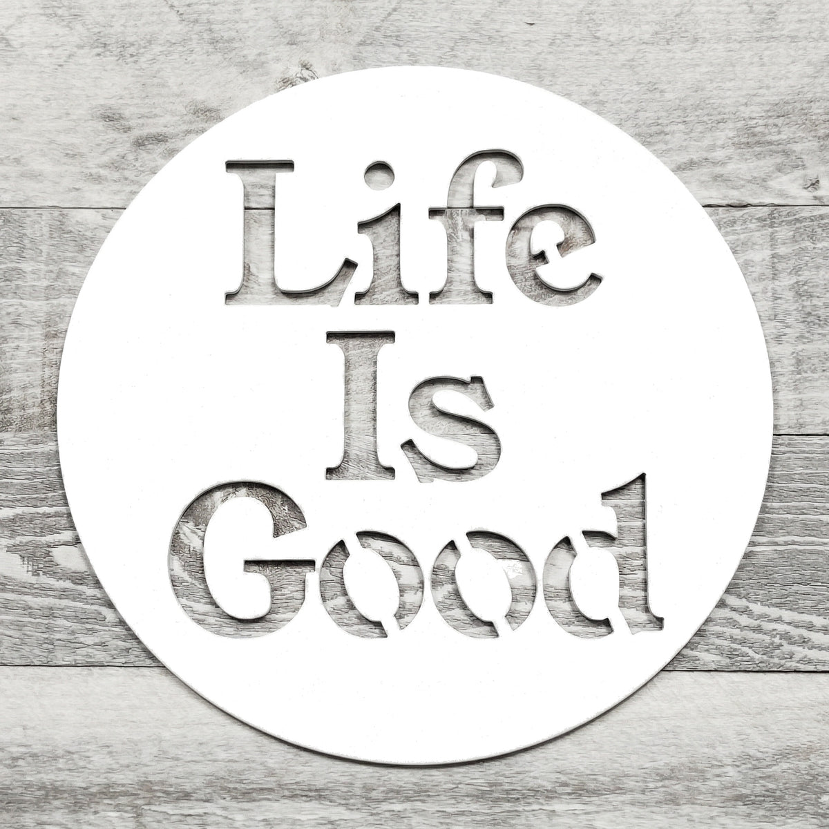 white circular metal sign with 'Life Is Good' text on a wooden background