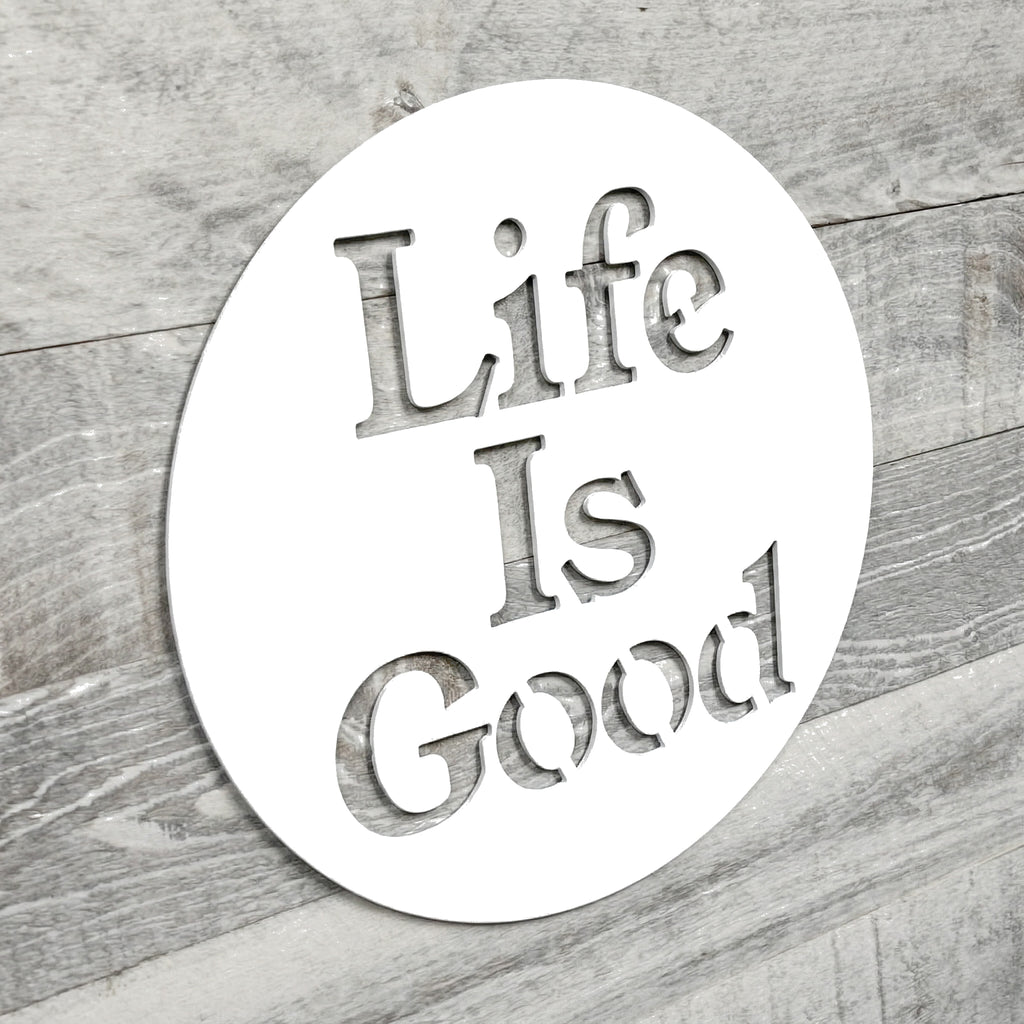 Circular metal sign with 'Life Is Good' text on a wooden surface