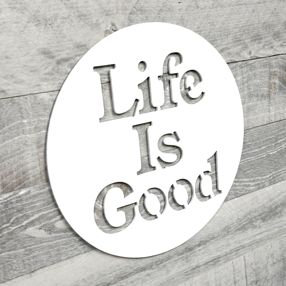 Circular metal sign with 'Life Is Good' text on a wooden surface