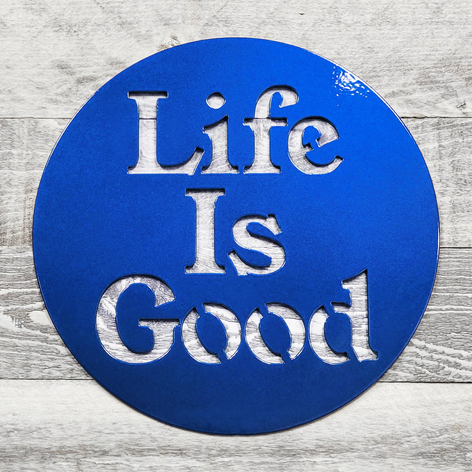 Blue circular sign with 'Life Is Good' text on a wooden surface