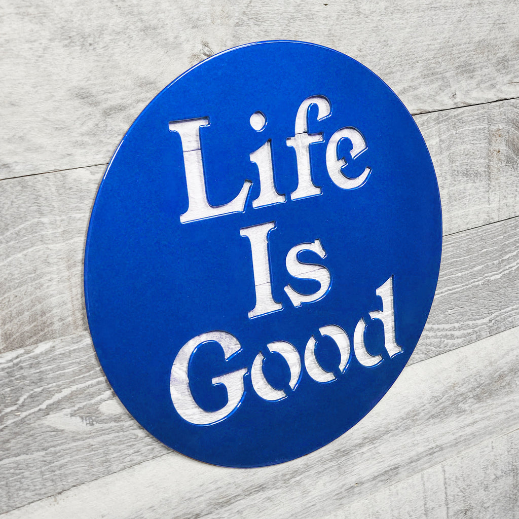 Blue circular sign with 'Life Is Good' text on a wooden surface