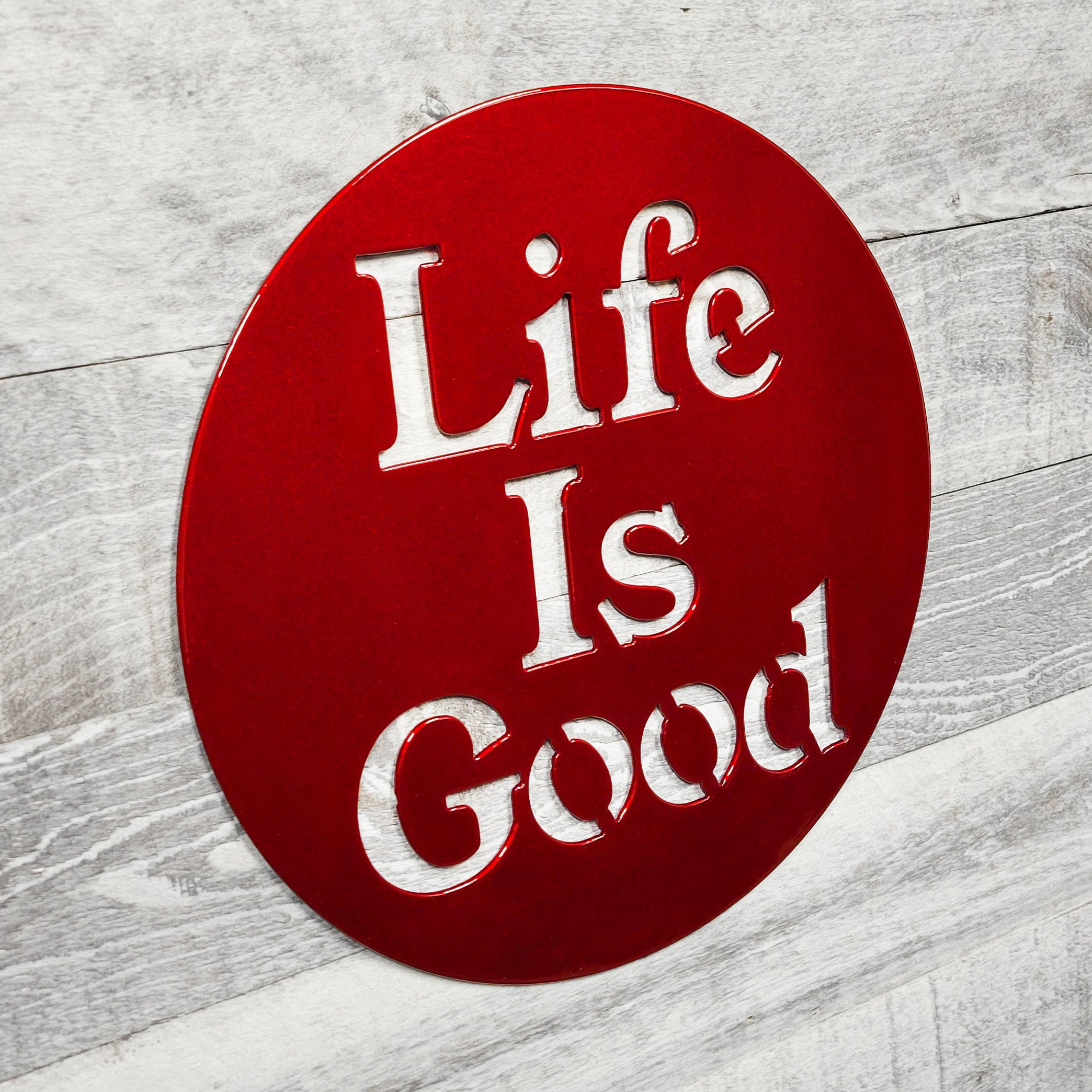 Red circular sign with 'Life Is Good' text on a wooden surface