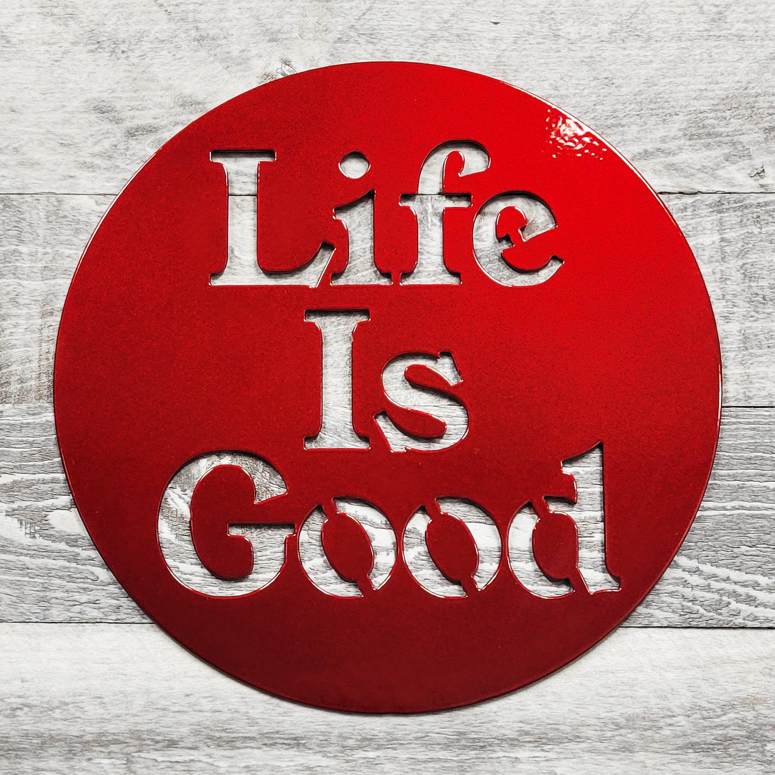 Red circular sign with 'Life Is Good' text on a wooden surface