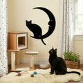 Black cat sitting on a white rug with a decorative wall art of a cat on a moon.