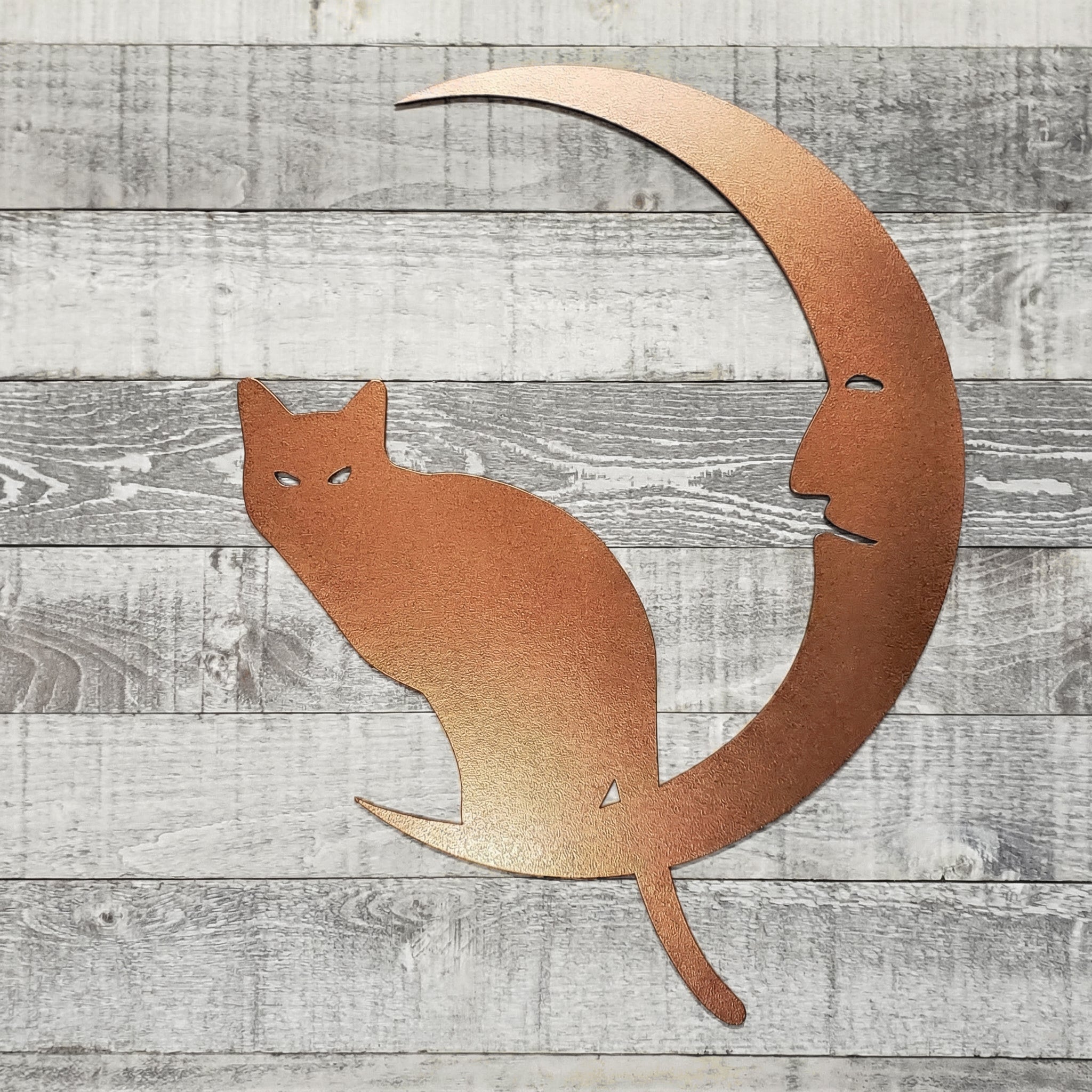 Decorative metal wall art of a cat on a crescent moon against a wooden background