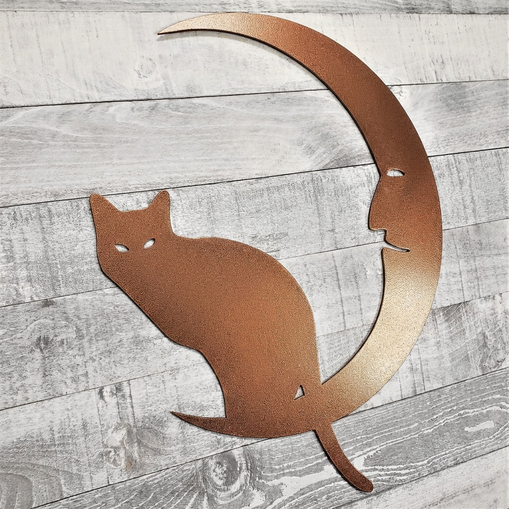 Decorative metal wall art of a cat on a crescent moon on a wooden surface