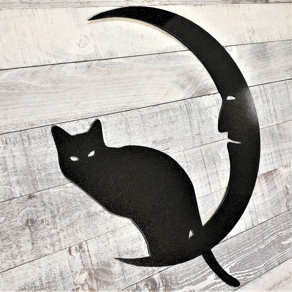 Black metal cat and crescent moon wall art on a wooden surface