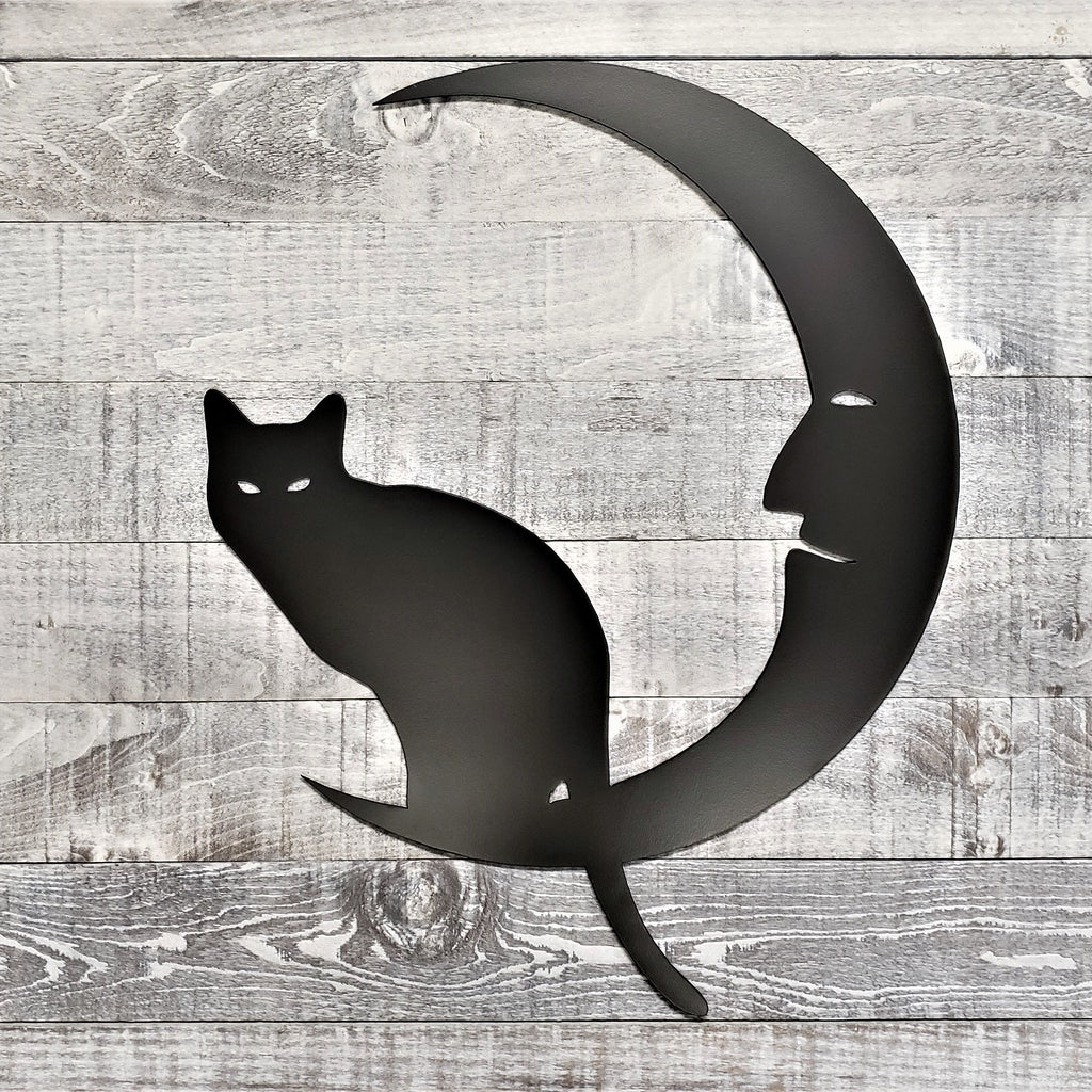 Decorative metal wall art of a cat on a crescent moon on a wooden background