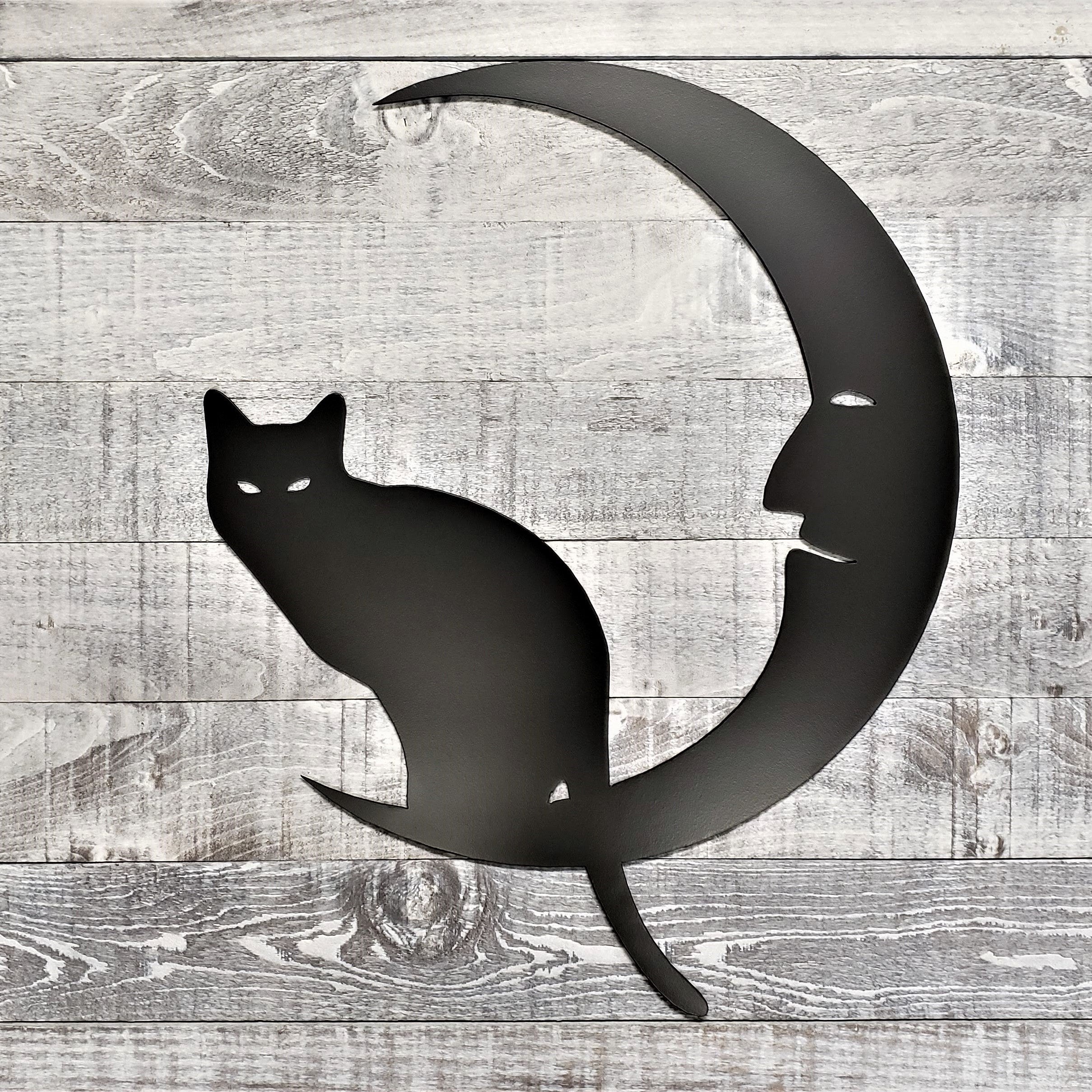 Decorative metal wall art of a cat on a crescent moon on a wooden background