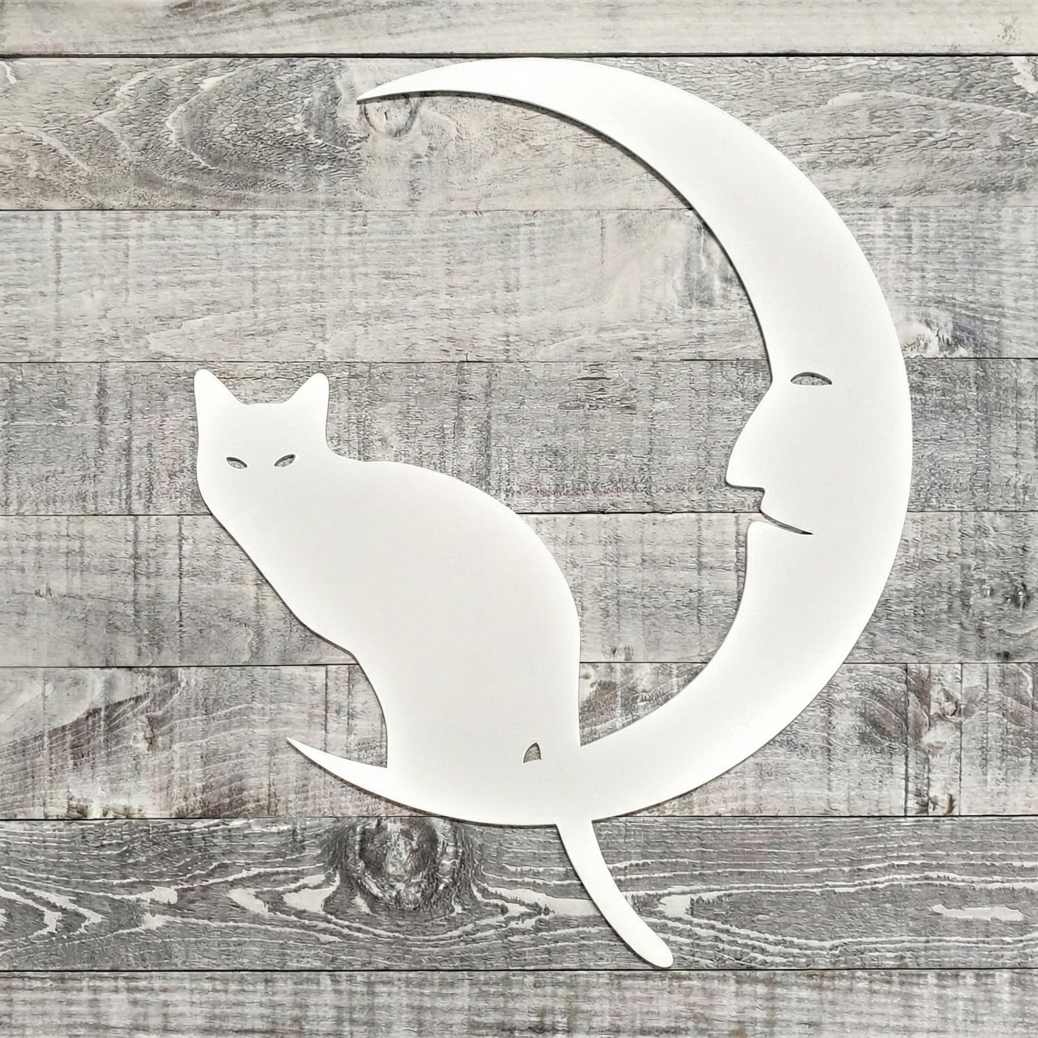 Decorative metal wall art of a cat on a crescent moon with a face, on a wooden background.