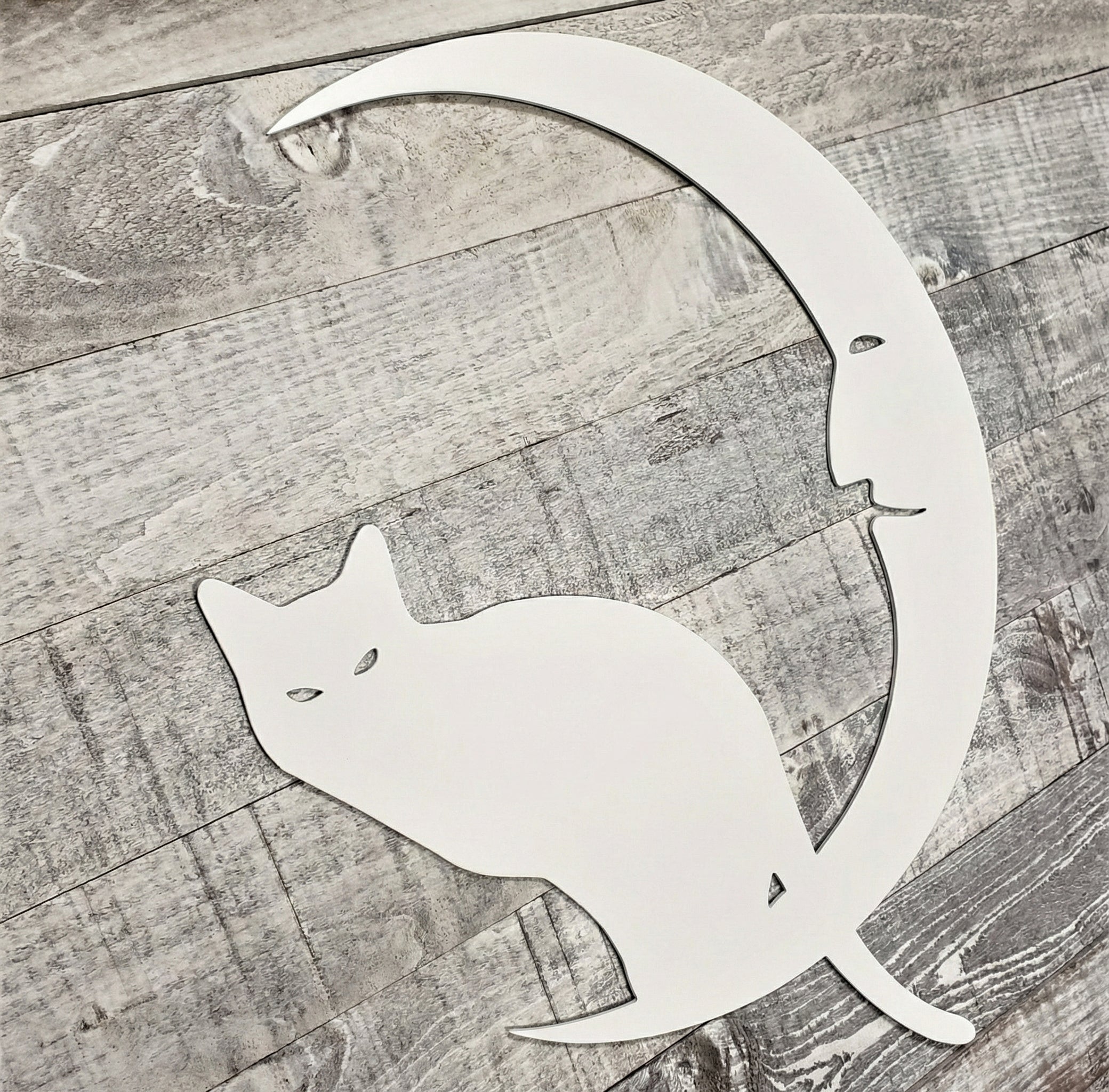 Decorative metal wall art of a cat and crescent moon on a wooden surface