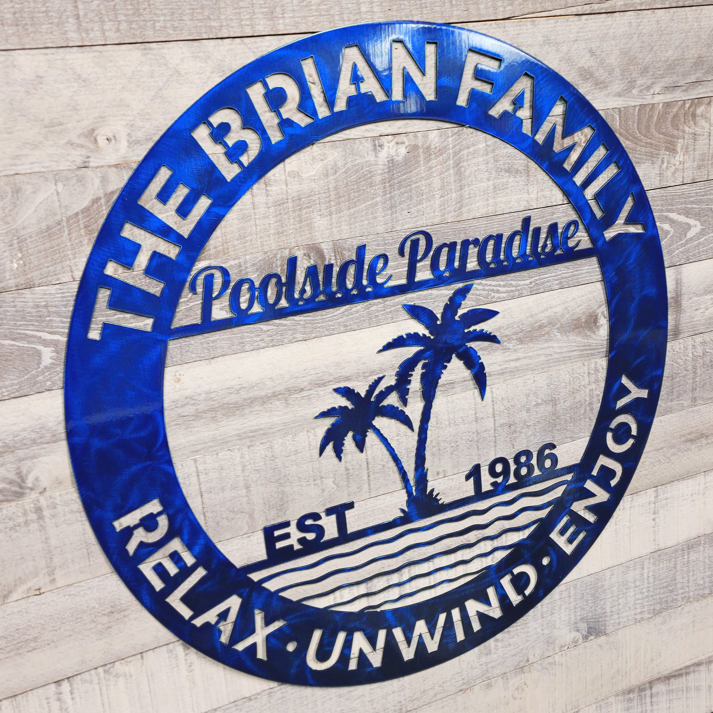 Blue circular Family Poolside Paradise metal wall art text on a wooden background