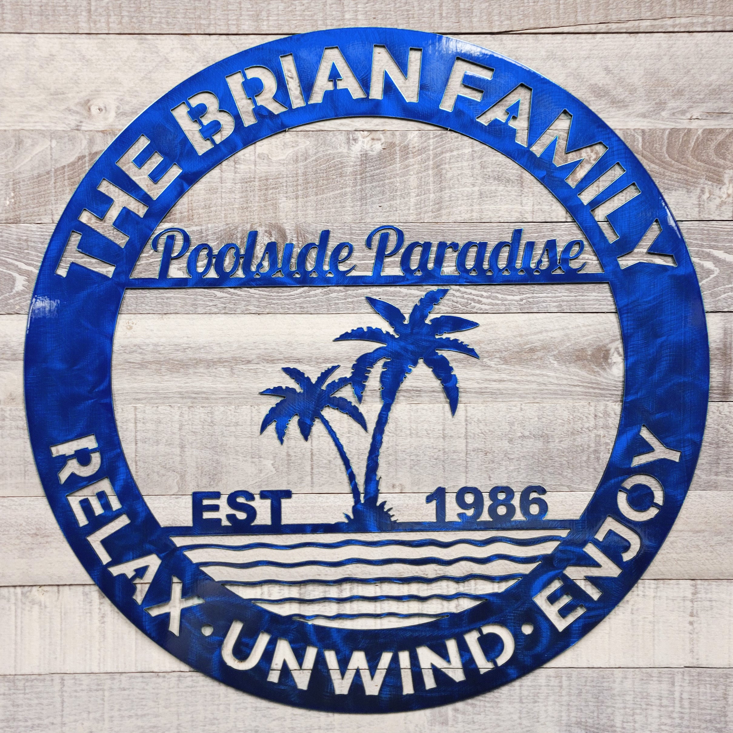 Blue circular poolside paradise metal wall art on a wooden background