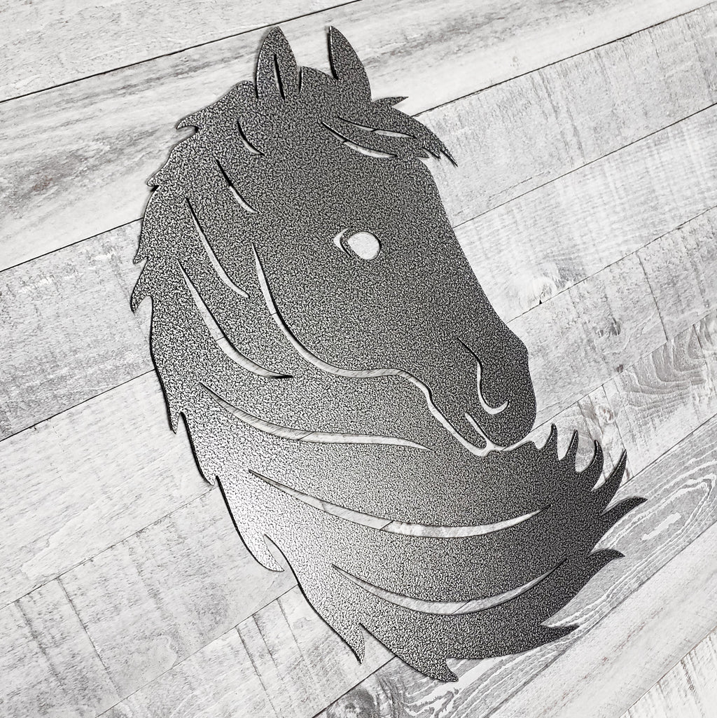 Black and silver metal horse head wall art on a wooden surface