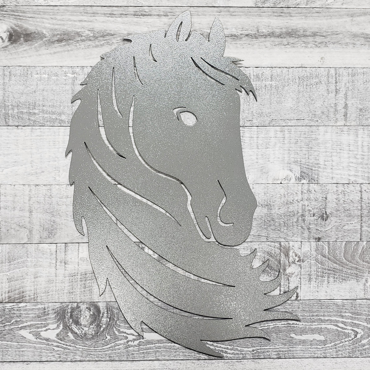 Silver metal horse head wall art on a wooden surface