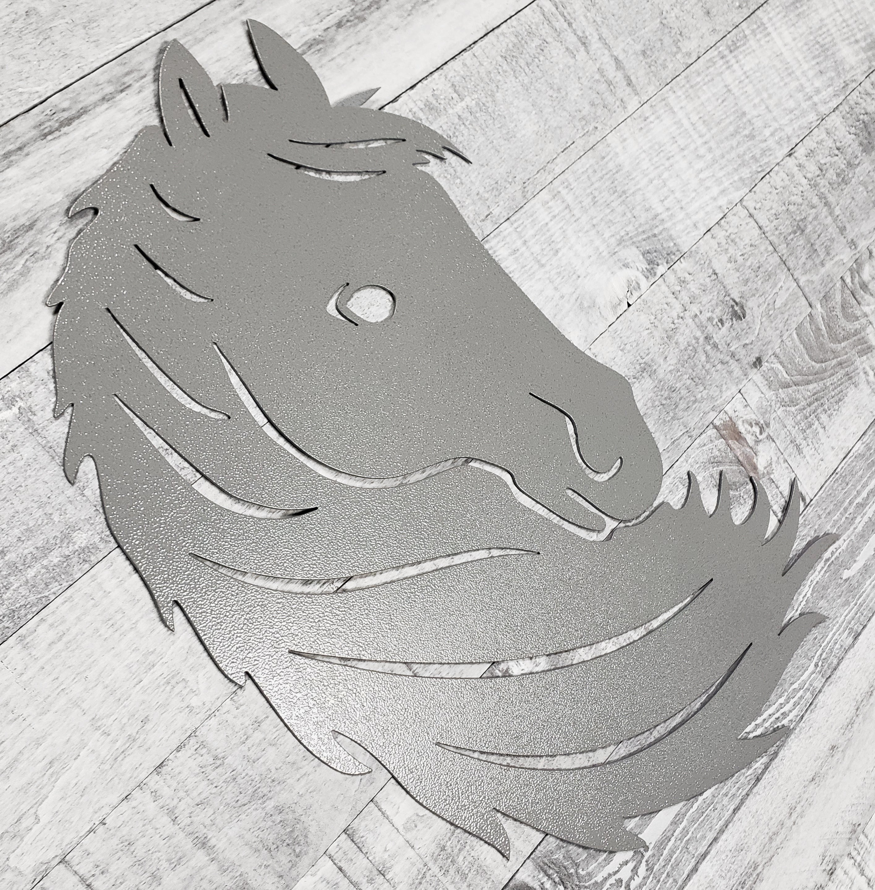 Silver metal horse head wall art on a wooden surface