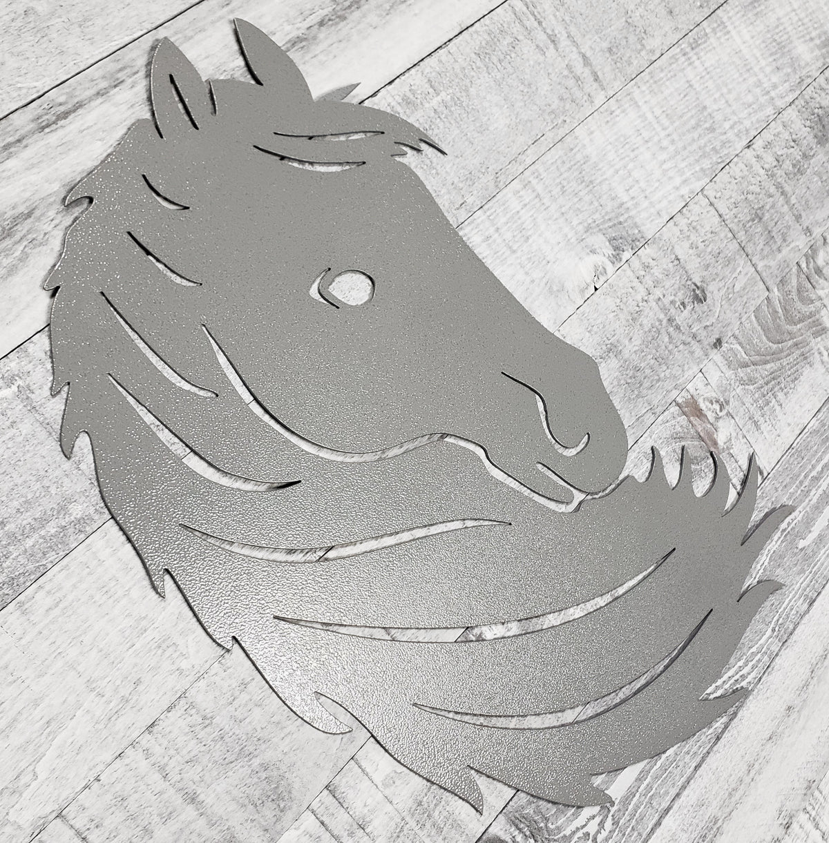 Silver metal horse head wall art on a wooden surface