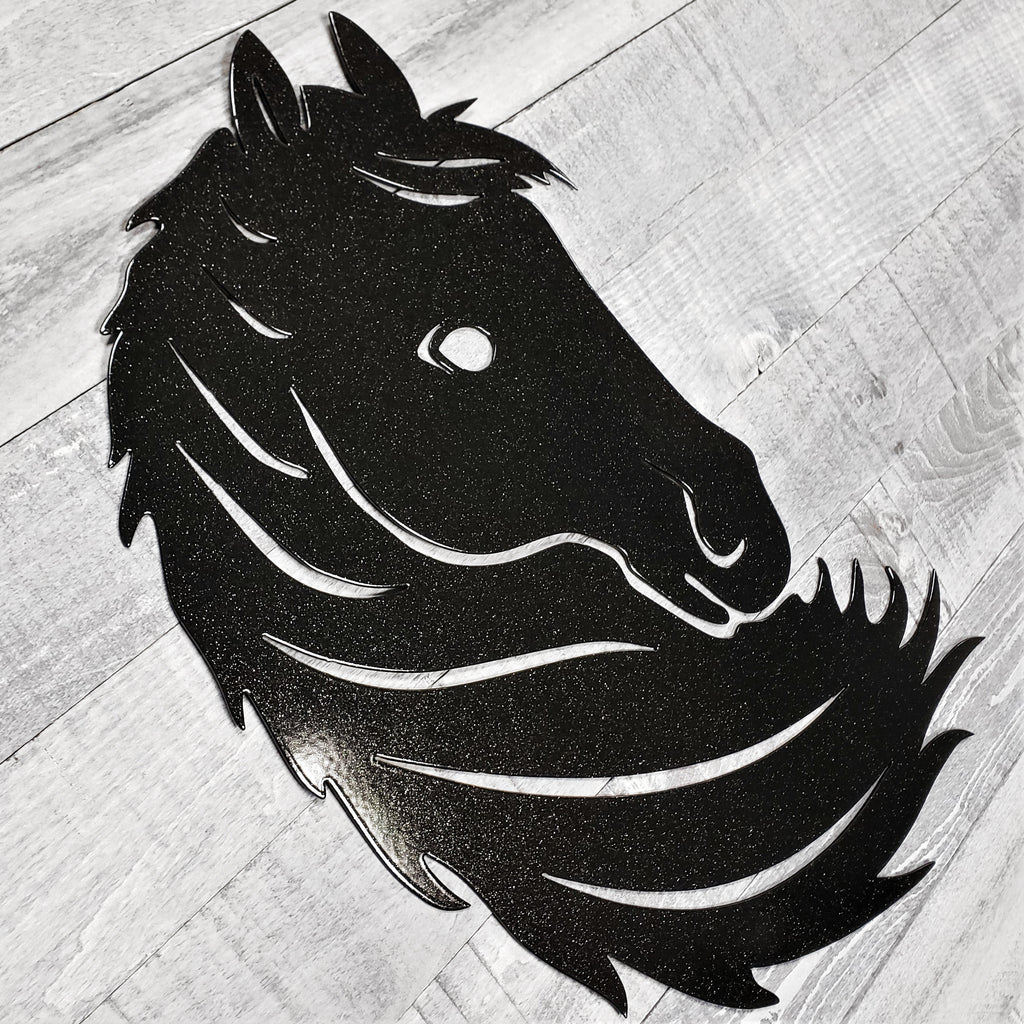 Black metal horse head wall art on a wooden surface