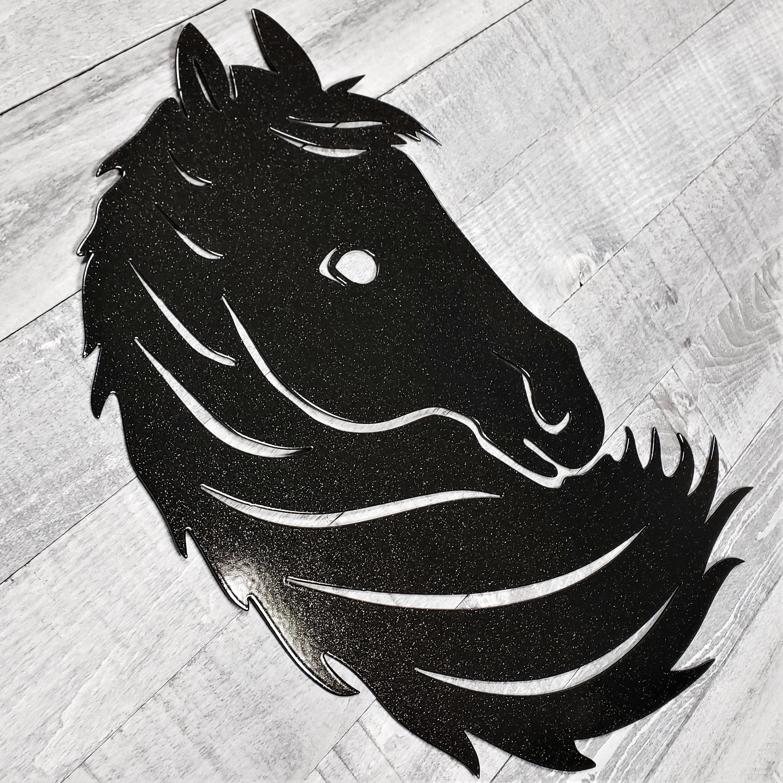 Black metal horse head wall art on a wooden surface