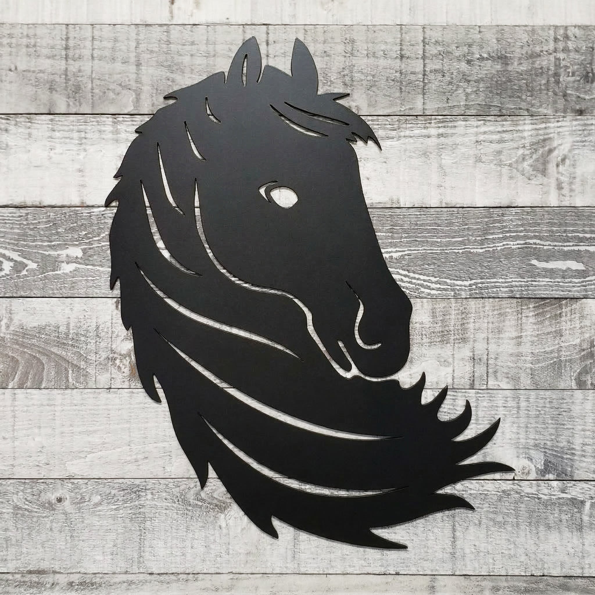 Black metal horse head wall art on a wooden surface
