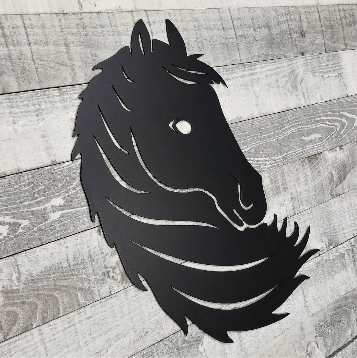 Black metal horse head wall art on a wooden surface