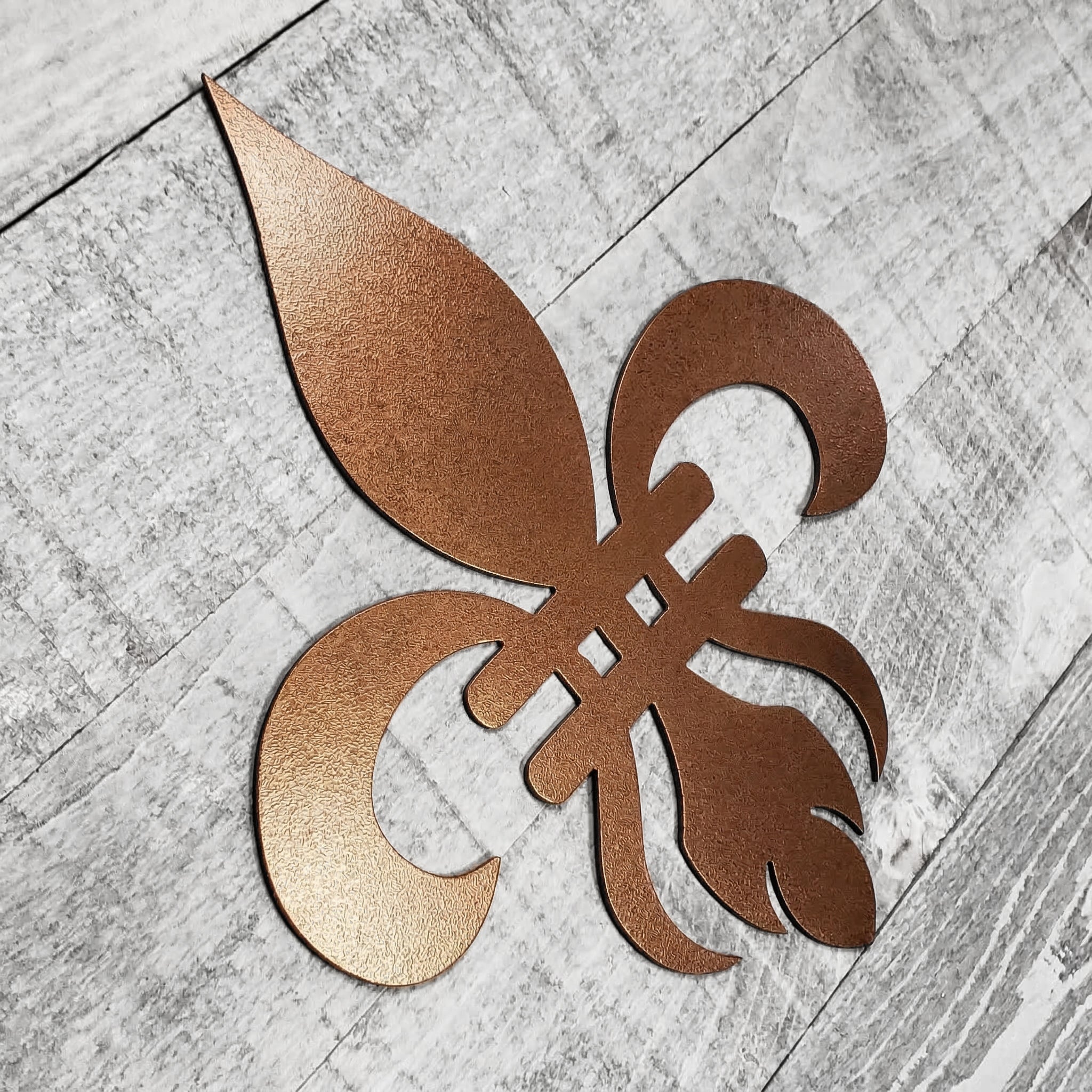 Decorative copper-colored metal fleur-de-lis on a wooden background