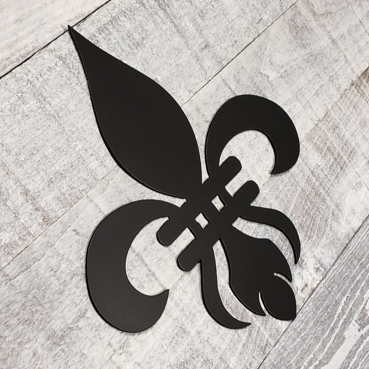 Decorative black metal fleur-de-lis on a wooden background