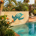 Decorative turtle sculpture on a stone wall by a pool with tropical plants.