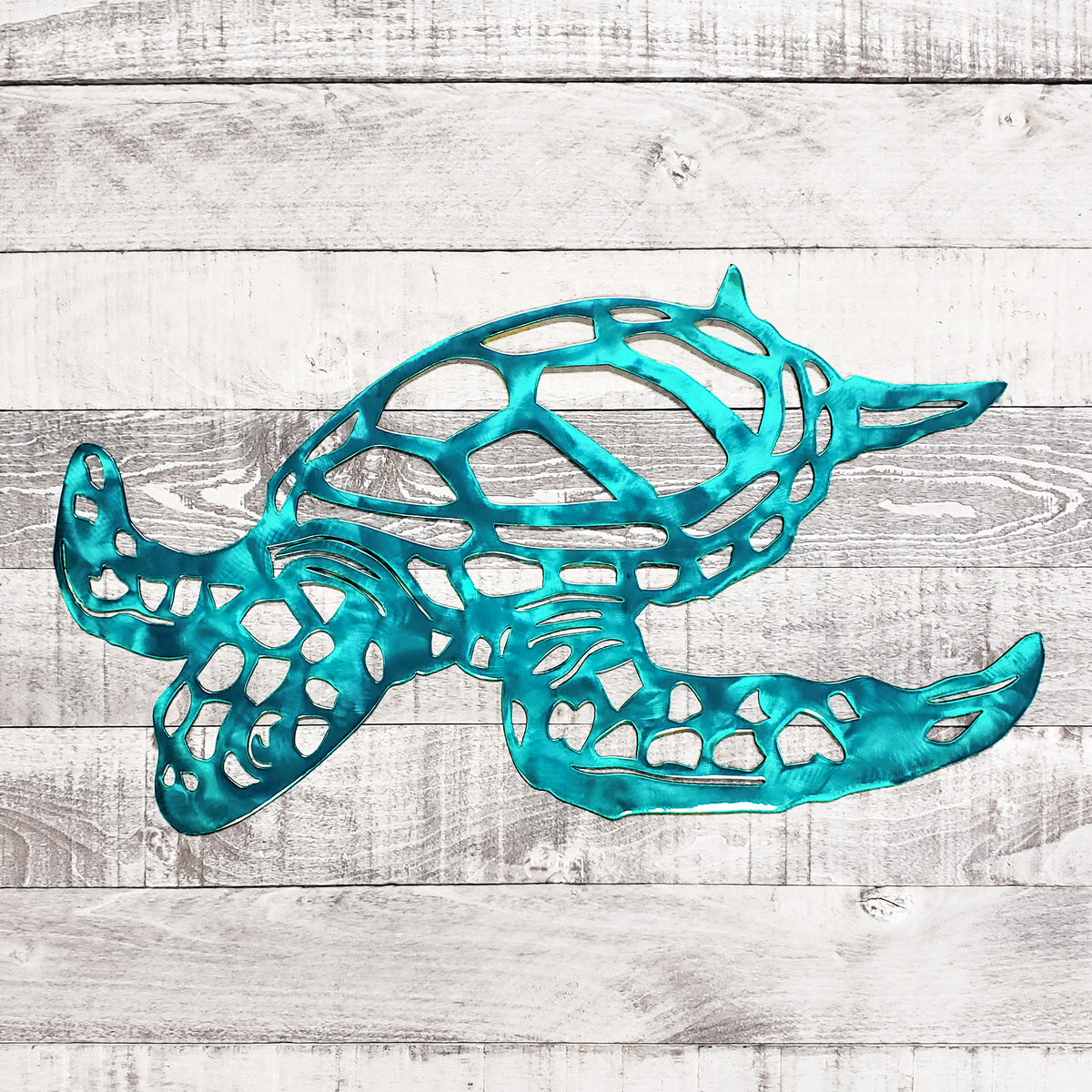 A turquoise metal sea turtle wall art piece with an openwork, geometric design, displayed against a rustic white-washed wood plank background.