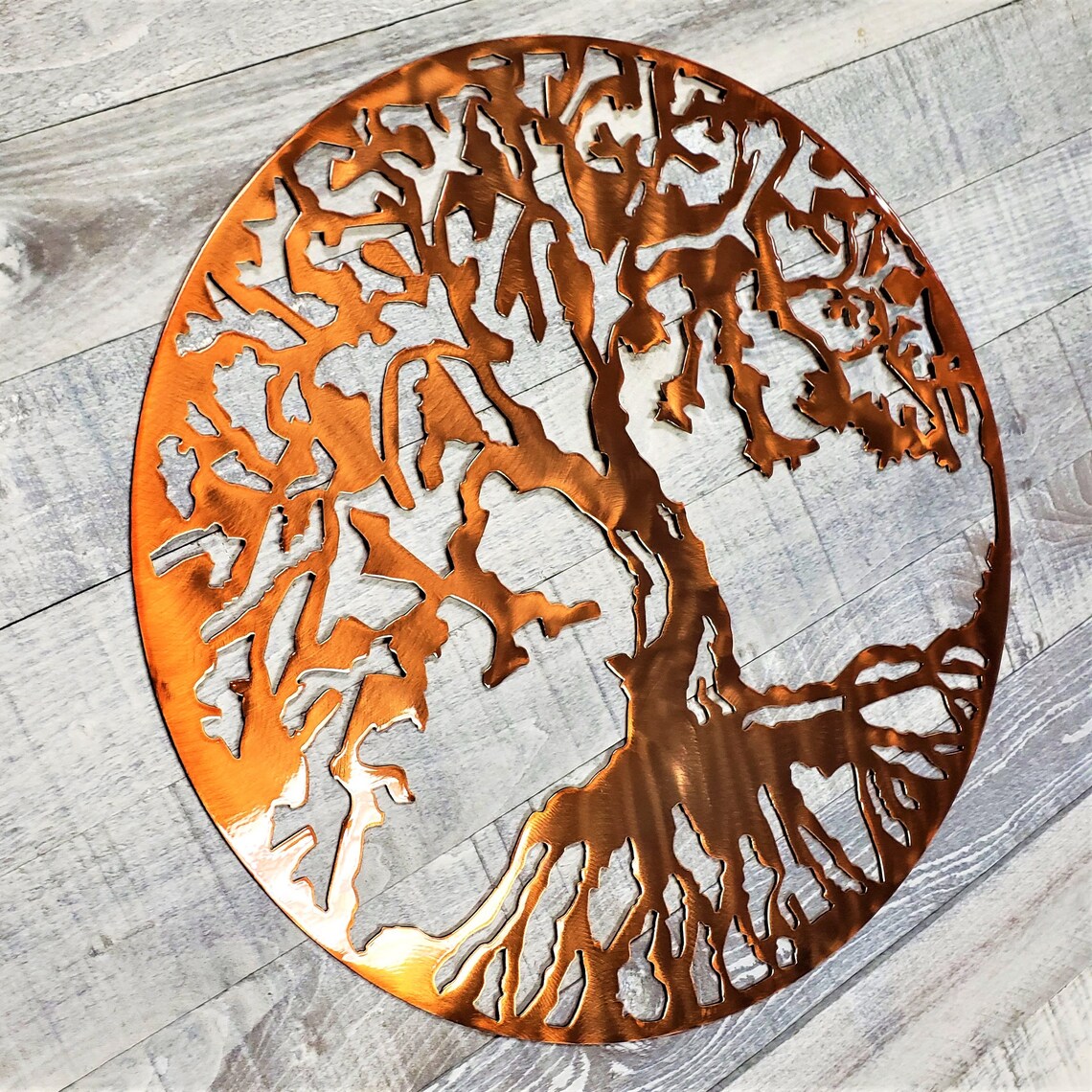Copper-colored metal wall art with tree design on a wooden surface