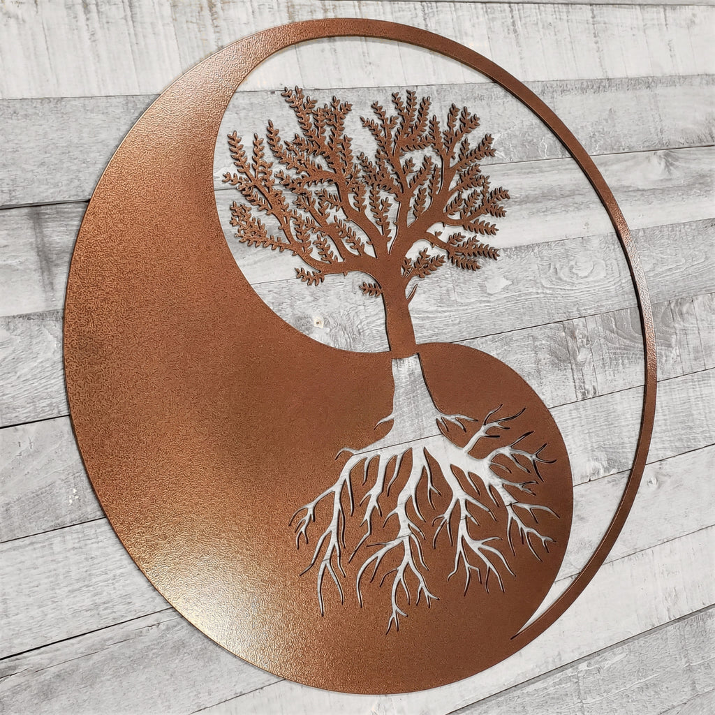 Decorative metal wall art with a tree design inside a yin yang symbol on a wooden surface.