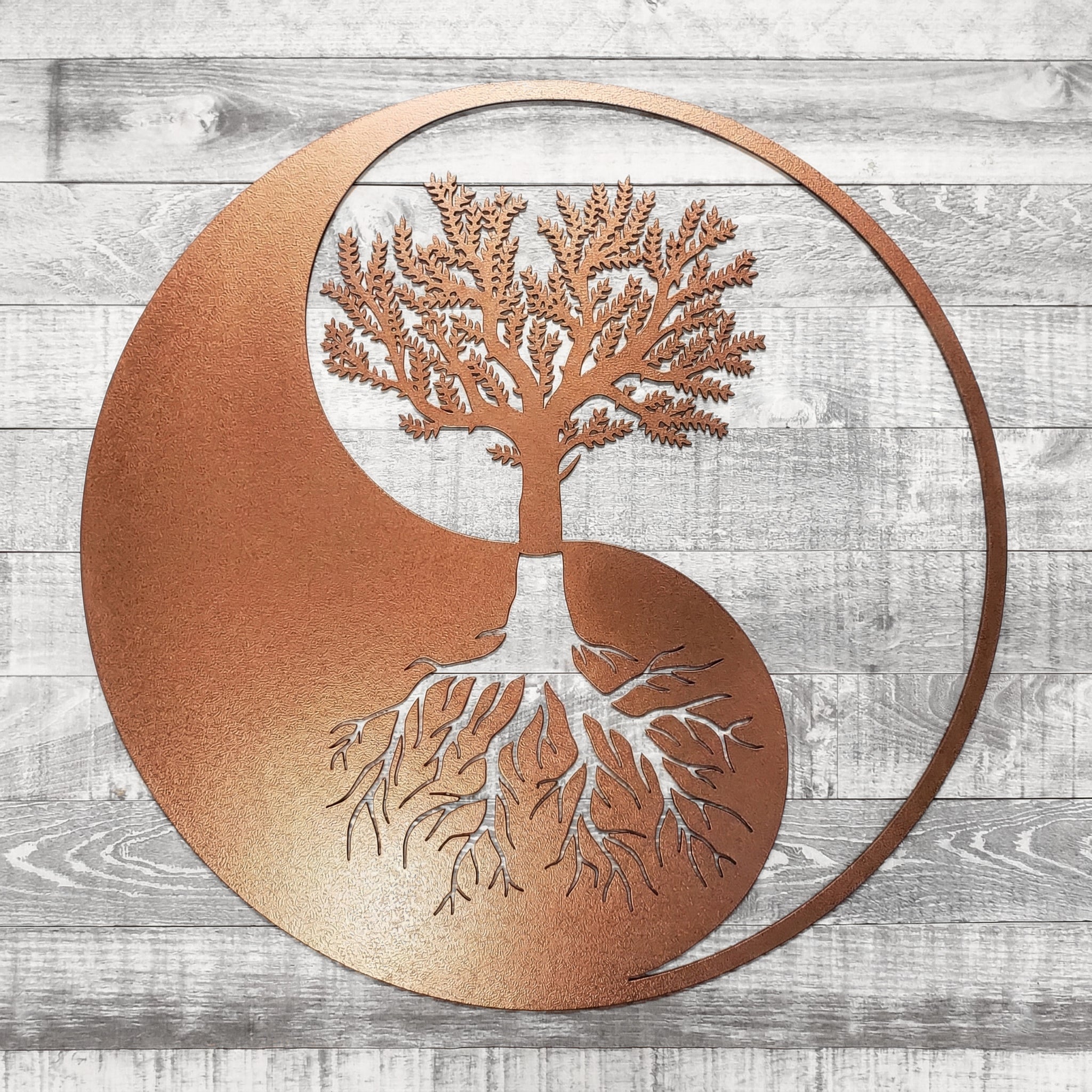 Metal wall art with a tree design inside a yin yang symbol on a wooden background